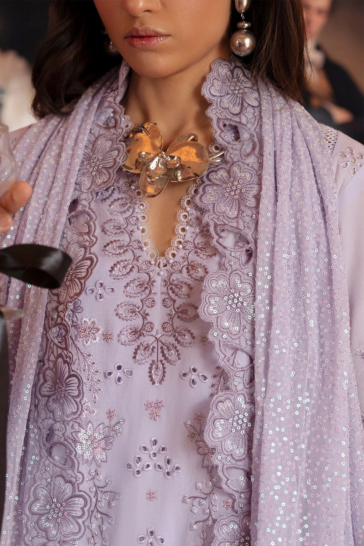 Woman wearing a light purple embroidered outfit with a matching scarf.