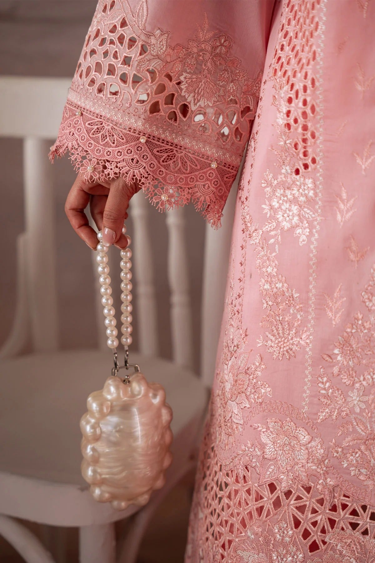Person wearing a pink embroidered garment holding a pearl-handled bottle.