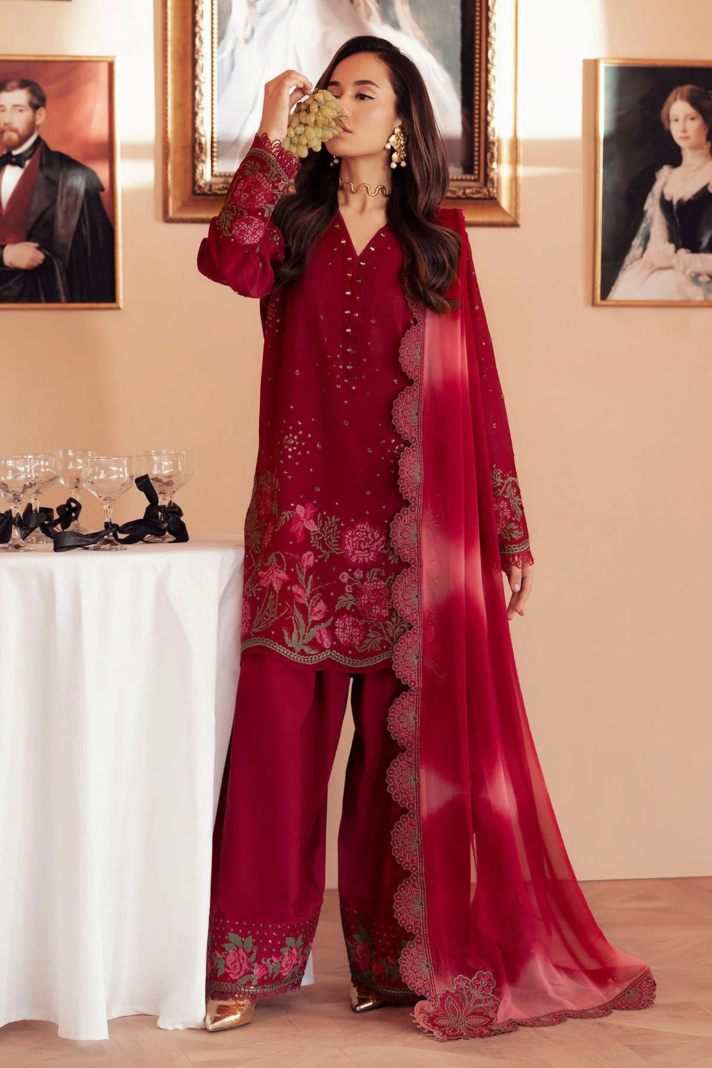 Woman in a red embroidered outfit standing in a room with framed pictures on the wall.