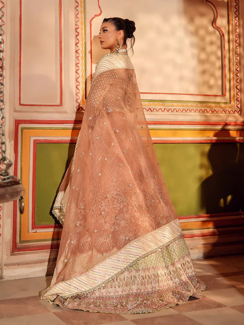 Woman in a traditional embroidered saree standing in a decorated room.