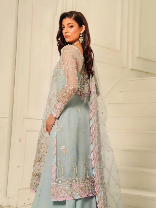 Woman wearing a light blue embroidered outfit against a white background