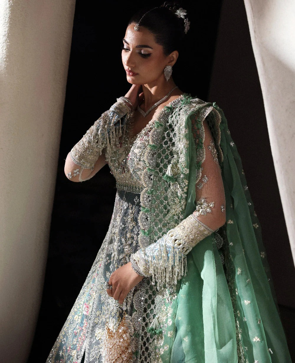 Woman in a traditional embroidered outfit with a green dupatta against a neutral background
