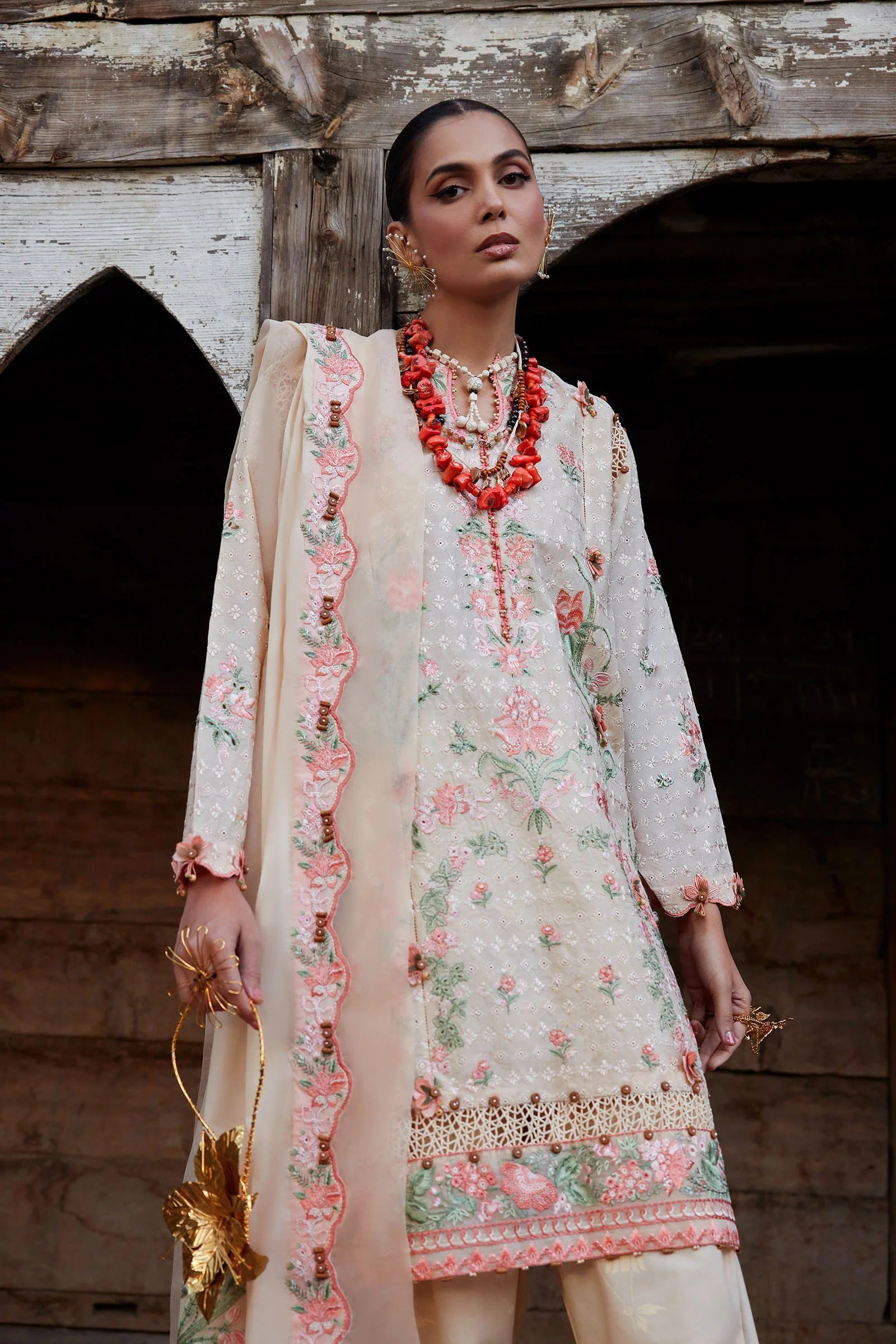 Woman in a floral embroidered outfit with jewelry against a rustic wooden background