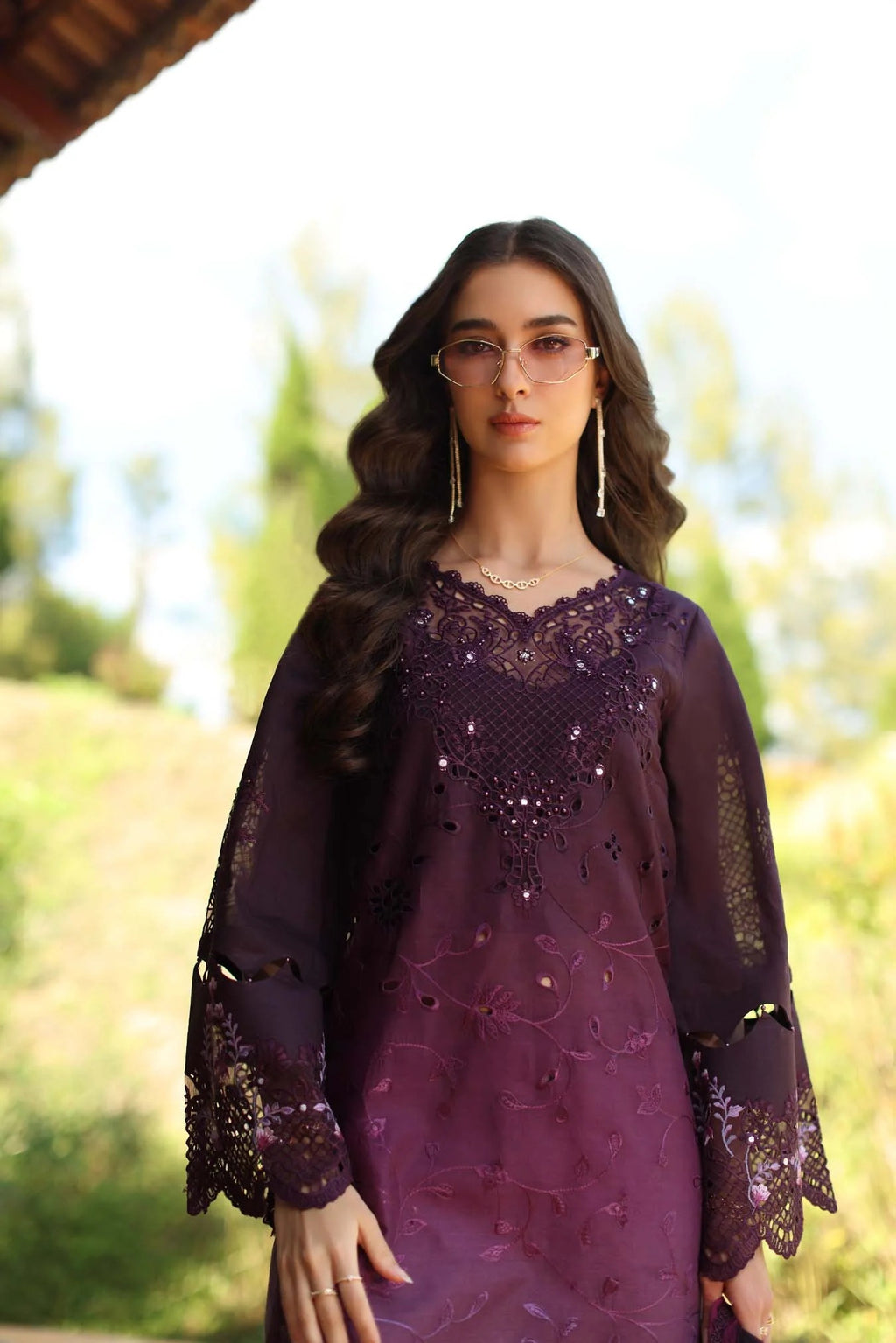 Woman wearing a dark purple embroidered dress with a blurred natural background