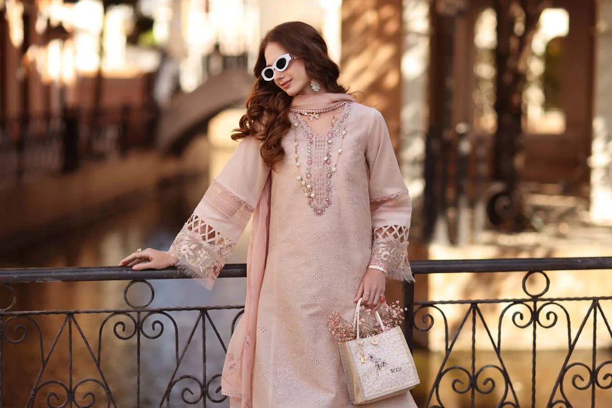 Woman in a light pink dress with lace details standing by a waterway.