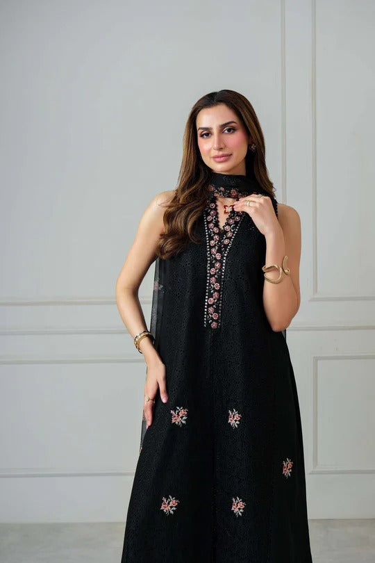 Woman wearing a black dress with floral embroidery against a white wall.