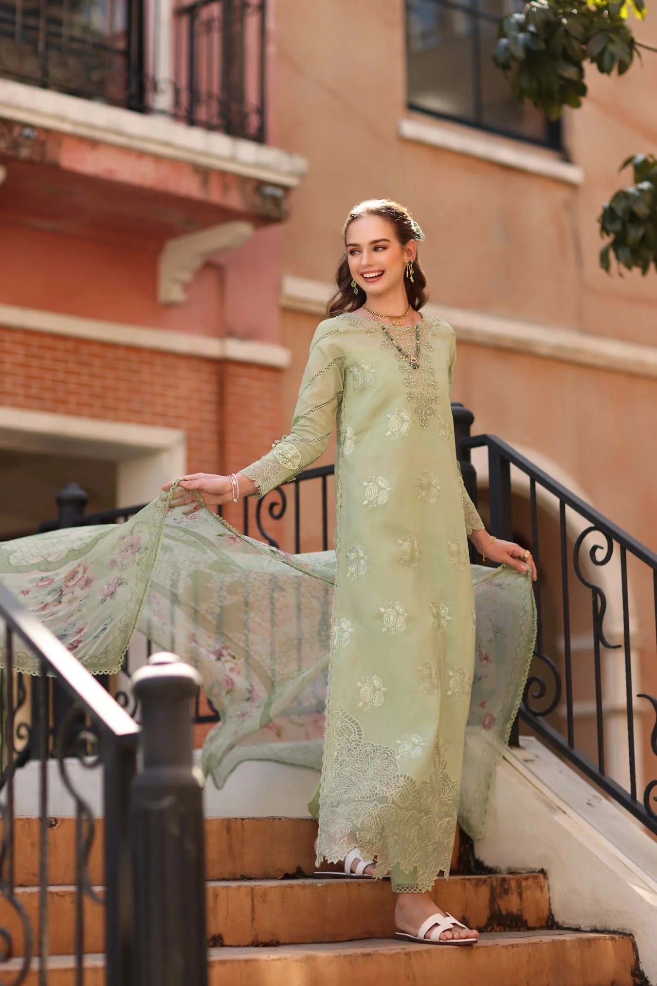 Woman in a light green traditional outfit standing on steps with a building in the background