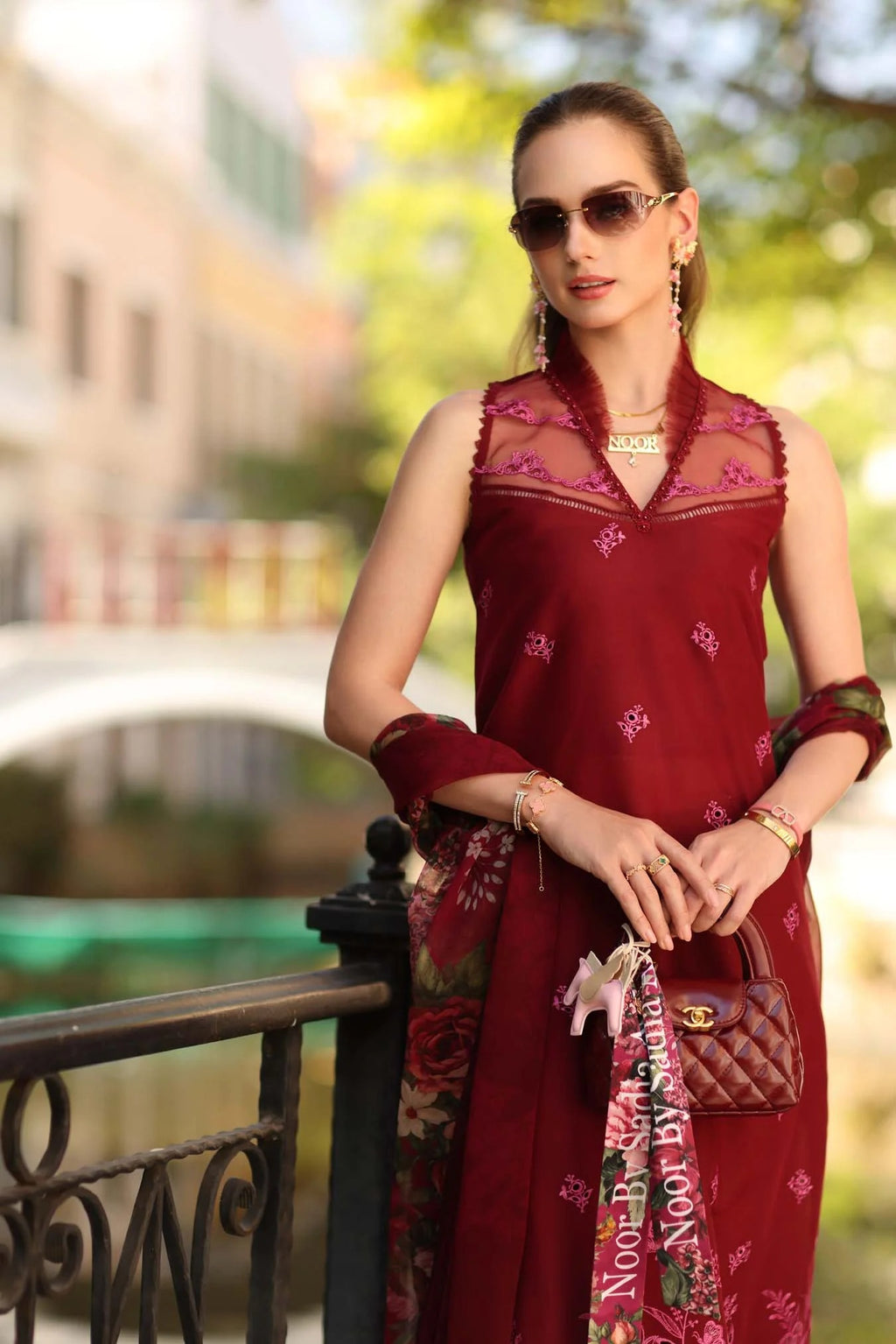 Woman in a red traditional outfit with sunglasses and a handbag, standing outdoors.