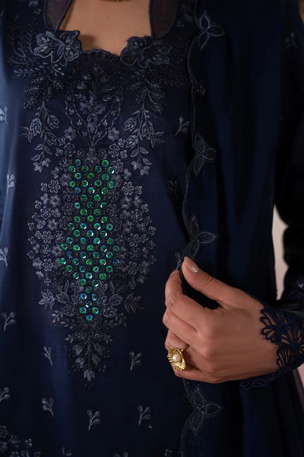 Navy blue embroidered garment with green gemstone details and a hand holding a phone.
