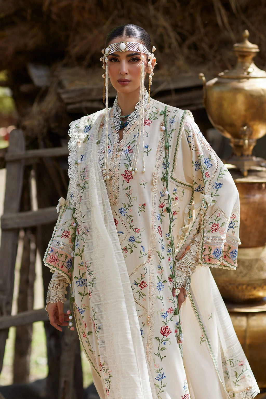 Woman in traditional embroidered outfit with intricate patterns, standing in a rustic setting.