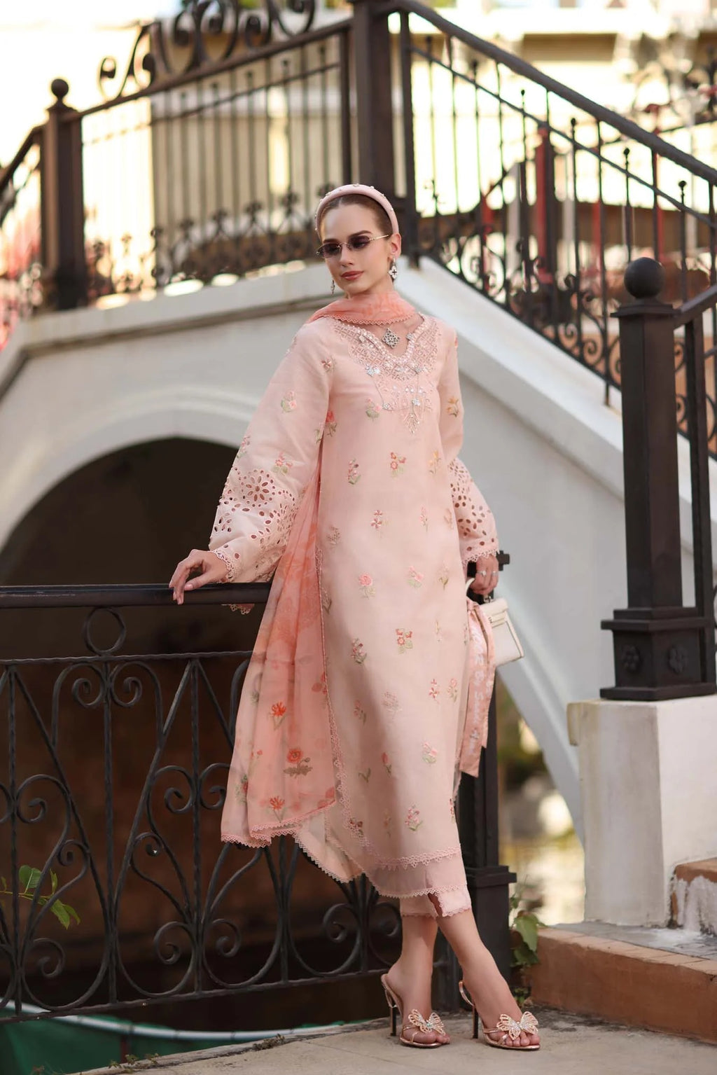 Woman in a peach embroidered outfit standing by a decorative metal railing.