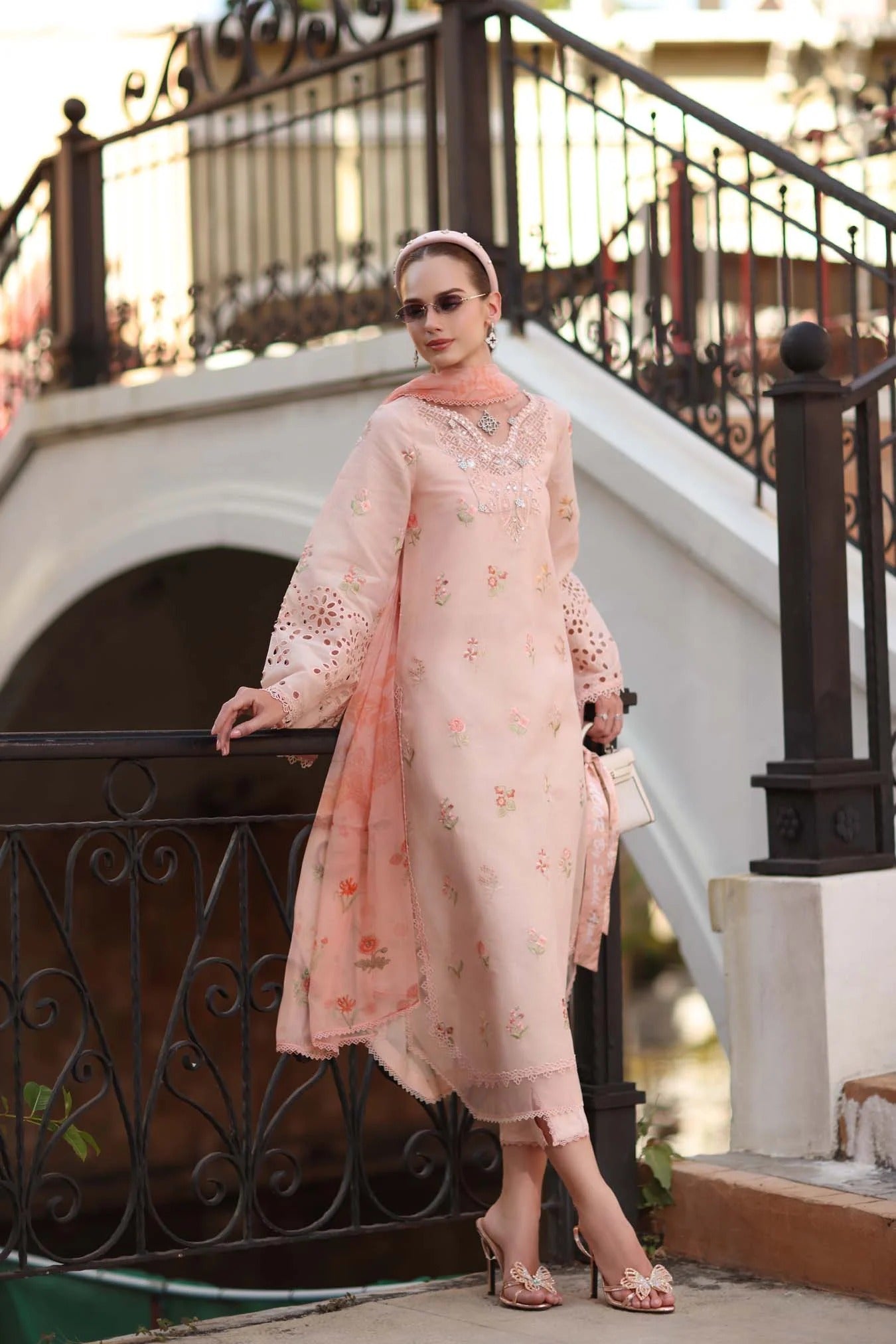 Woman in a peach embroidered outfit standing by a decorative metal railing.
