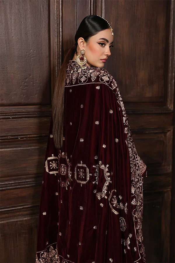 Woman in a maroon embroidered traditional outfit against a wooden paneled wall.