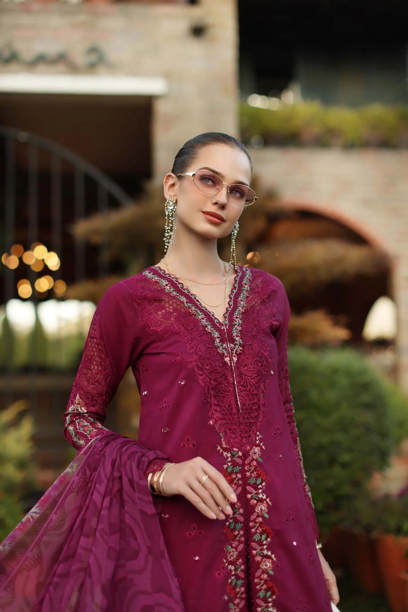 Woman in a magenta embroidered traditional outfit standing outdoors with blurred background