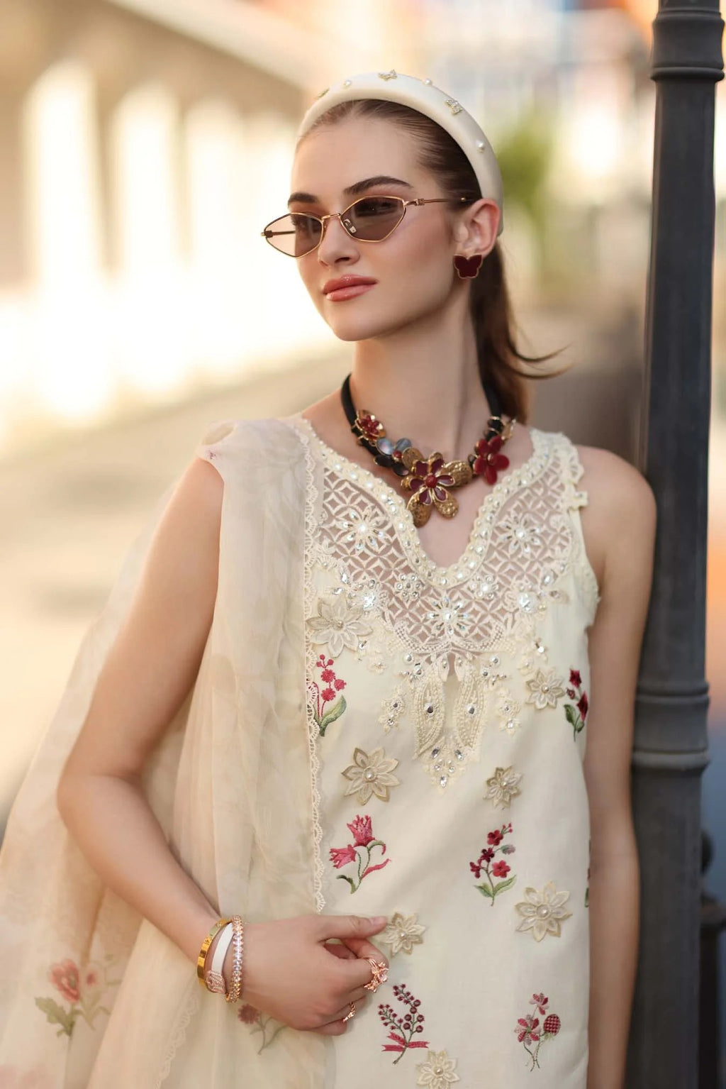 Woman wearing a cream embroidered dress with floral patterns outdoors.