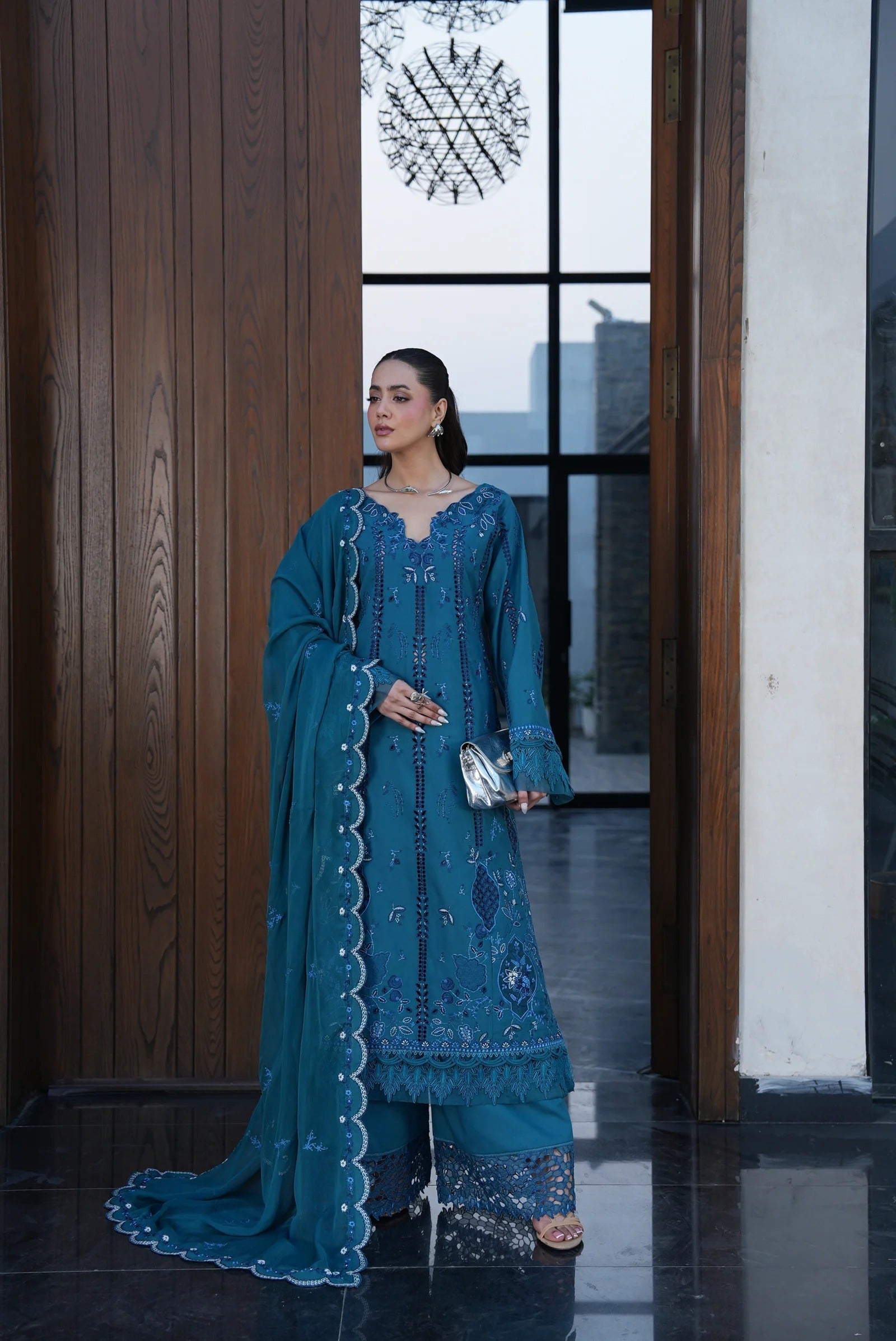 Woman in a blue embroidered outfit standing in a doorway.