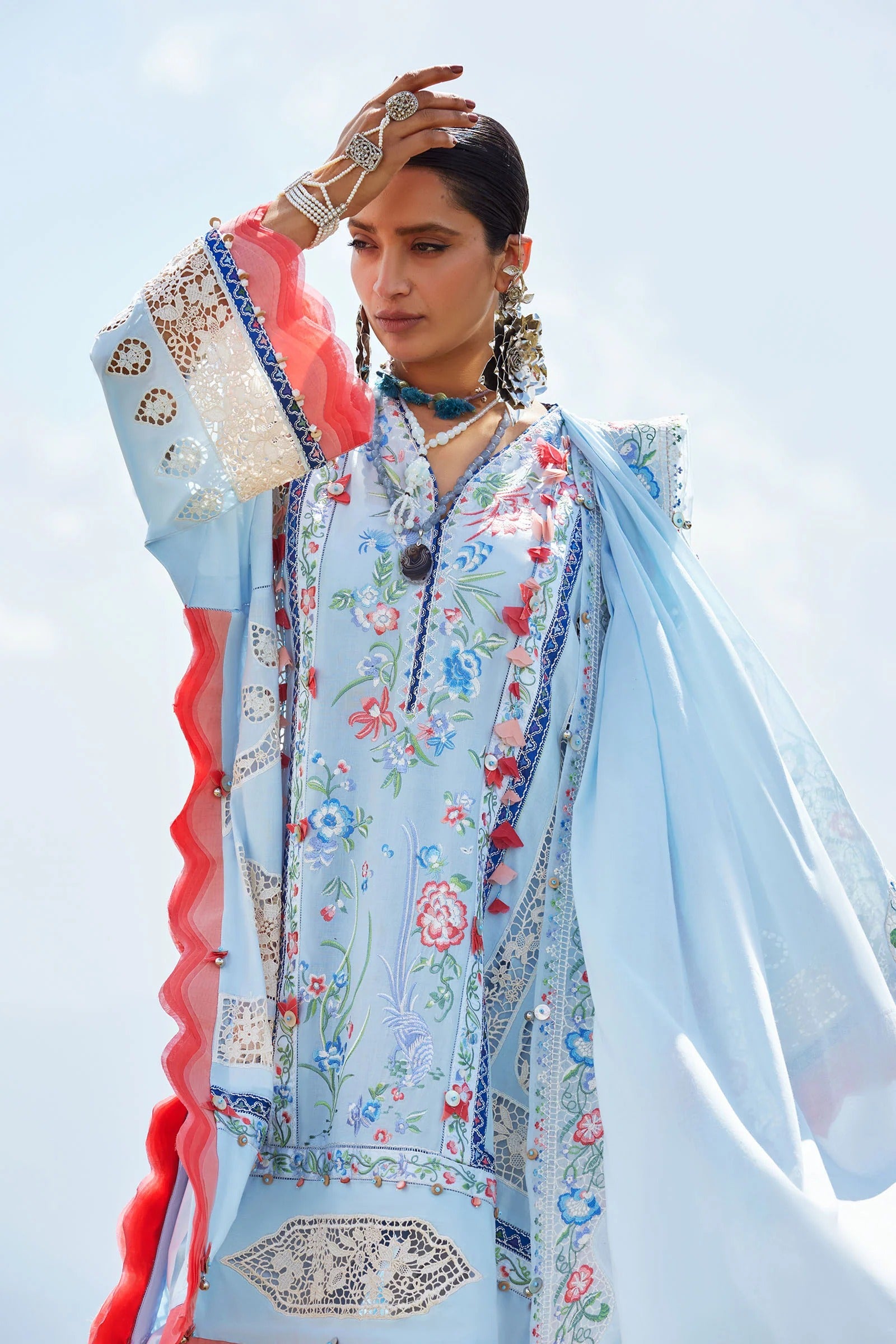 Woman wearing a traditional outfit with floral patterns and a light blue dupatta against a clear sky.