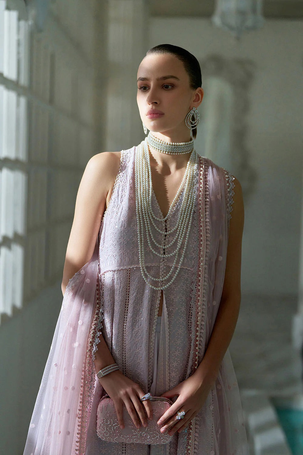 Woman in a light pink dress with pearl accessories in a softly lit room.