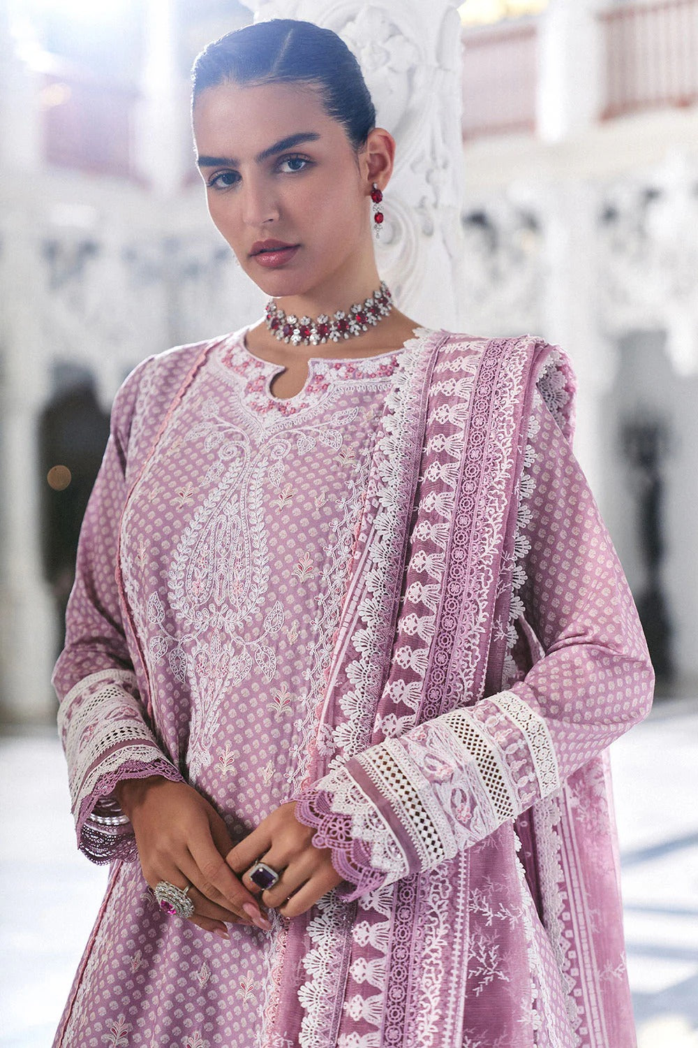 Woman wearing a pink embroidered traditional outfit with intricate patterns.