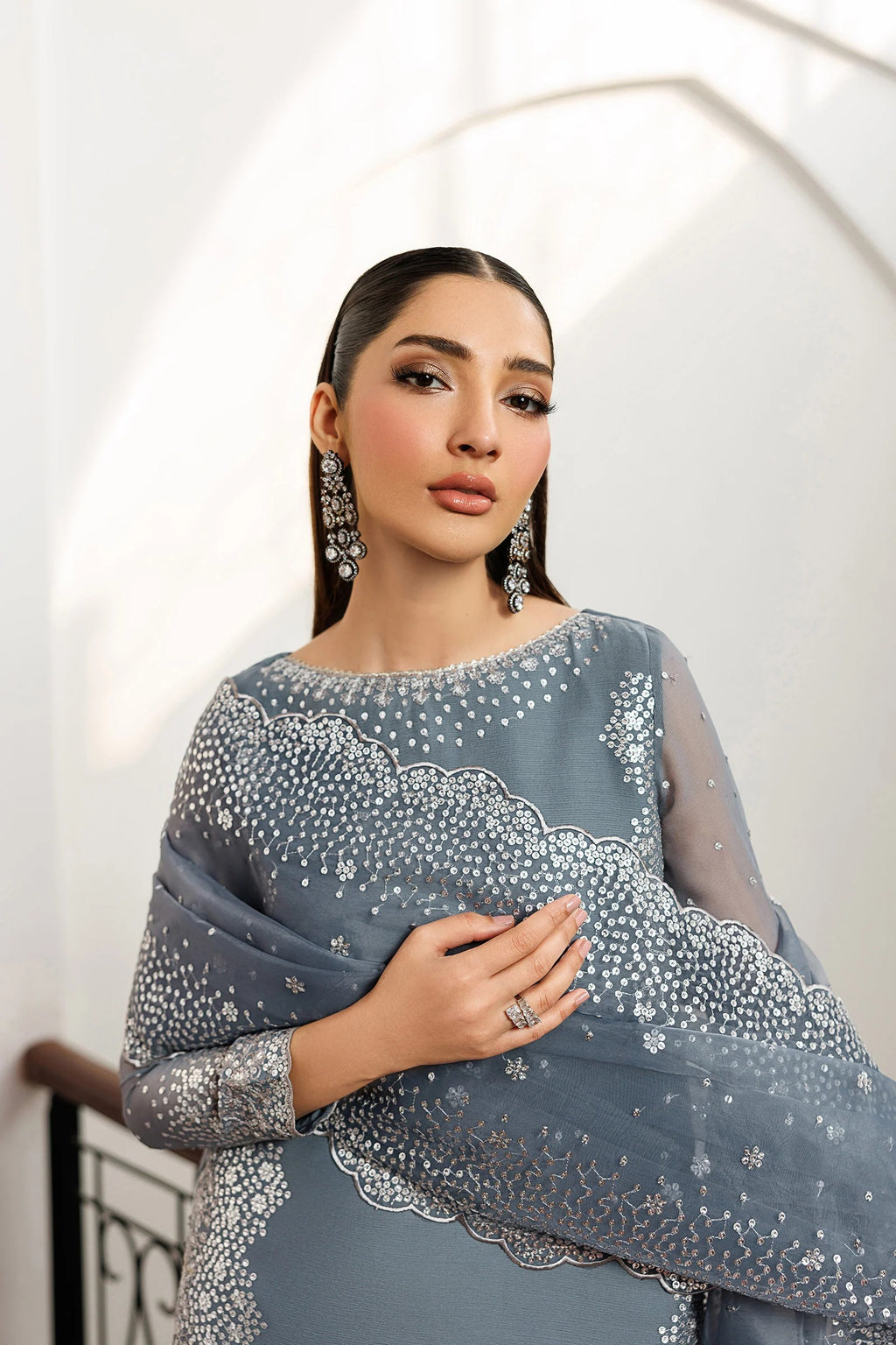 Woman wearing a gray saree with silver embroidery against a white background