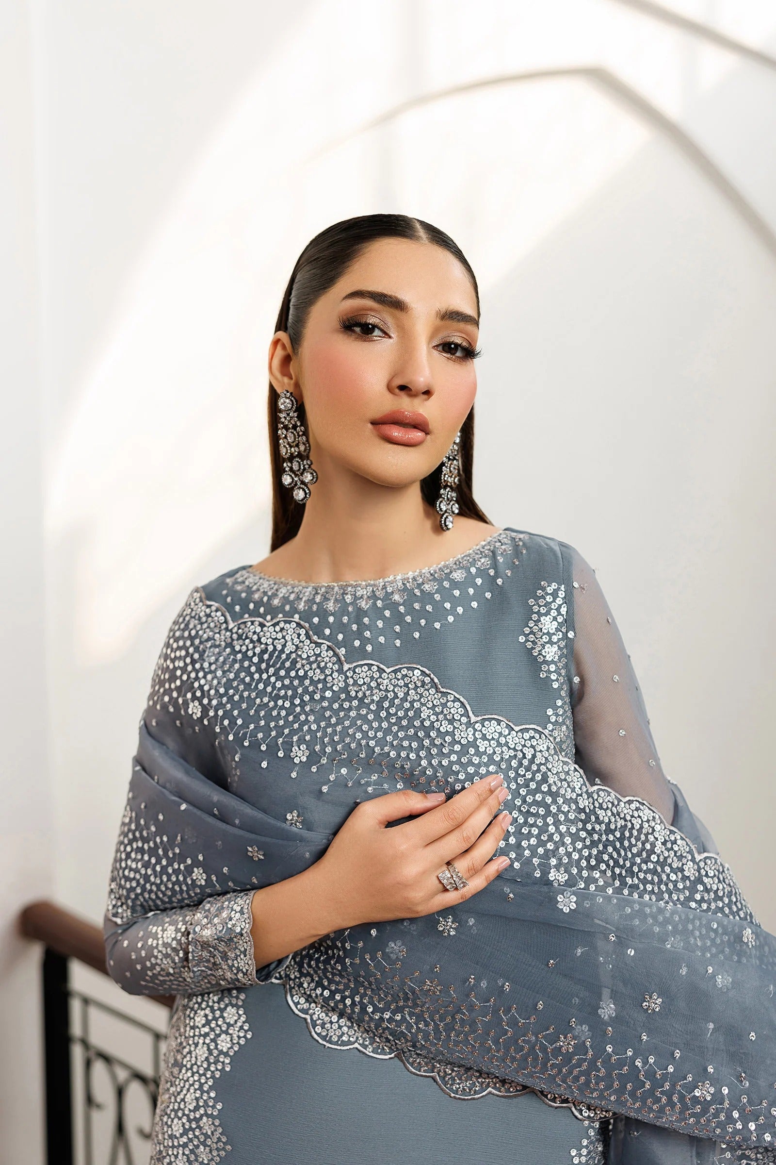 Woman wearing a gray saree with silver embroidery against a white background