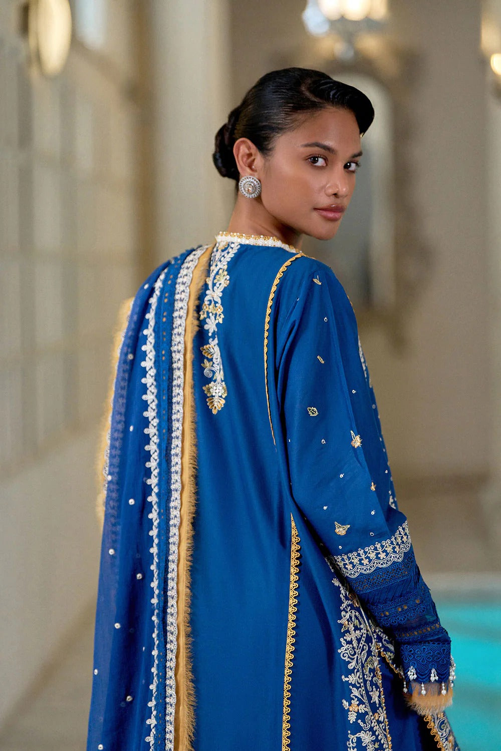 Woman wearing a blue embroidered traditional outfit in an elegant interior setting.