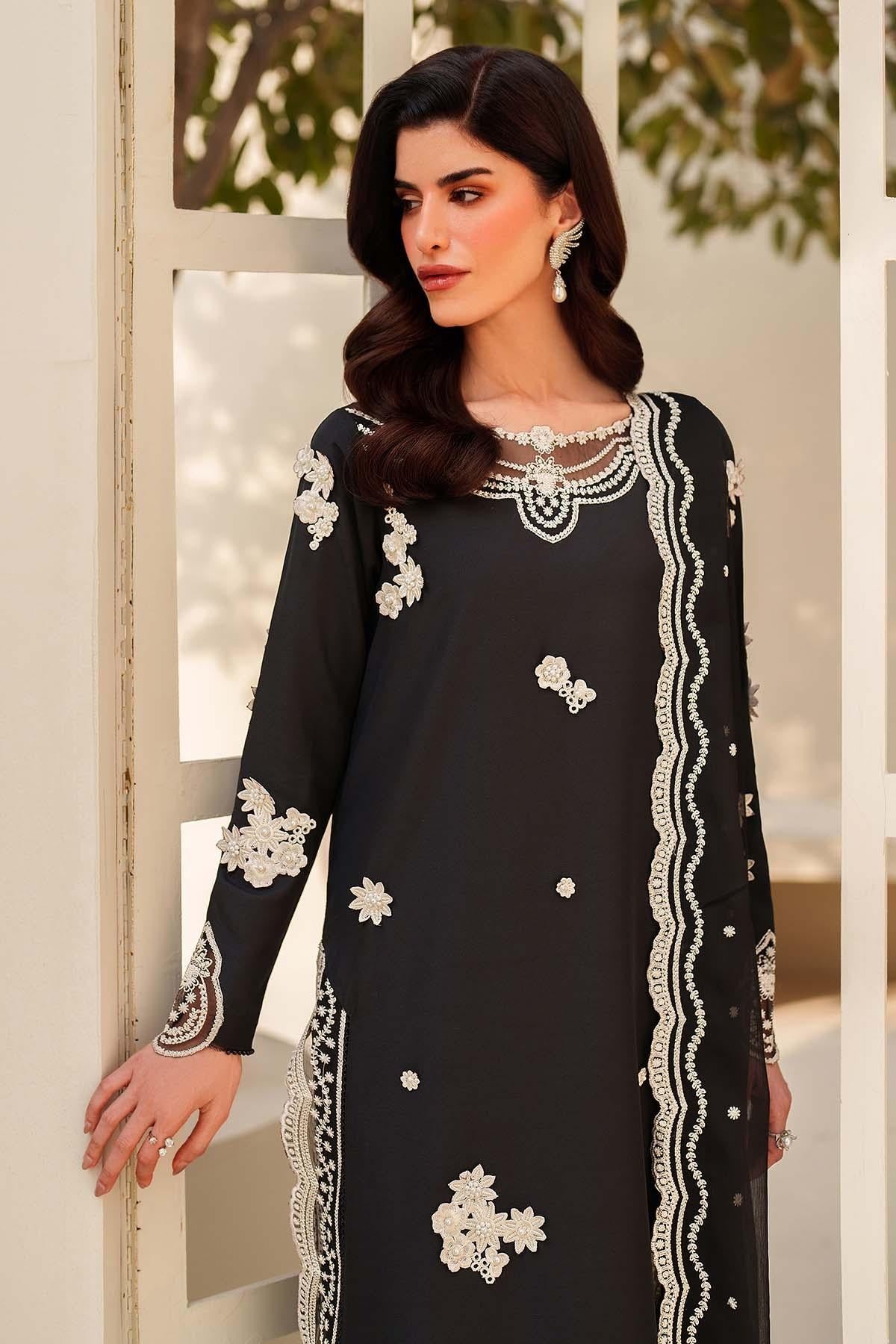 Woman wearing a black dress with white embroidery standing indoors.
