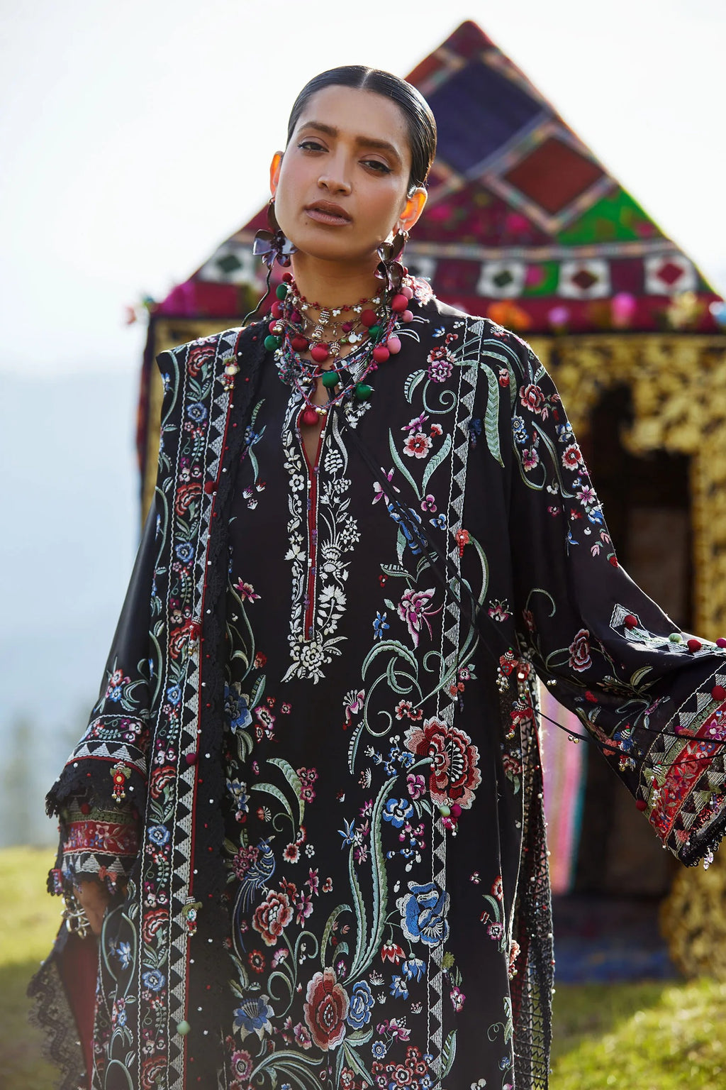 Woman wearing a black embroidered dress with colorful patterns in front of a decorative structure.