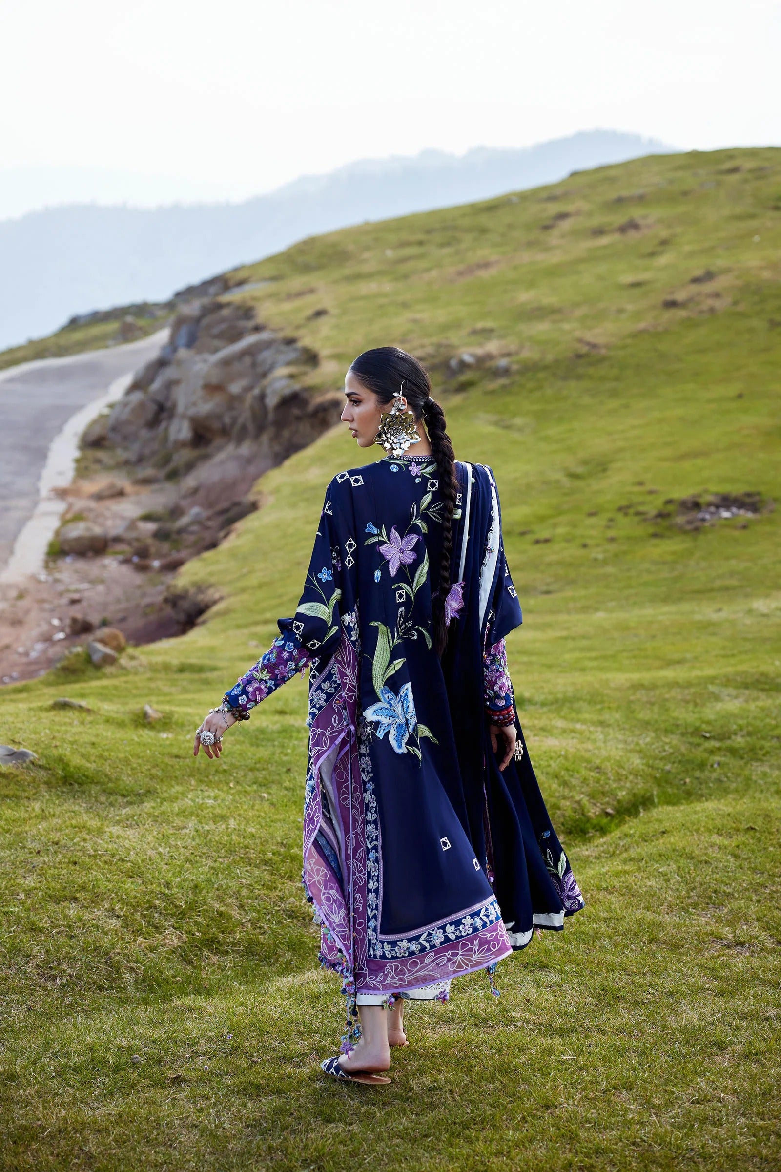 Woman in a floral dress standing on a grassy hillside with mountains in the background