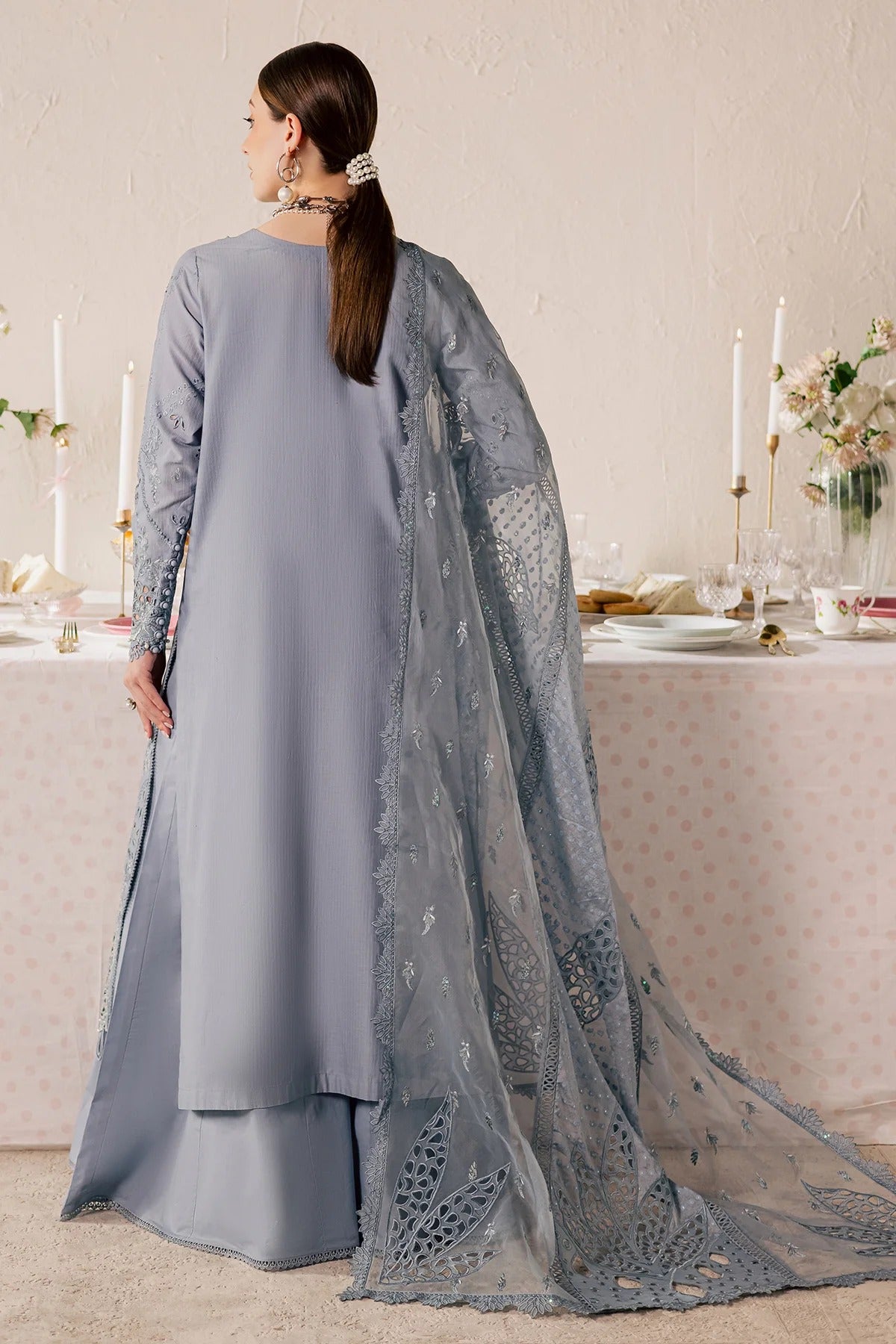 Woman in a gray dress with a long lace train standing in front of a decorated table.