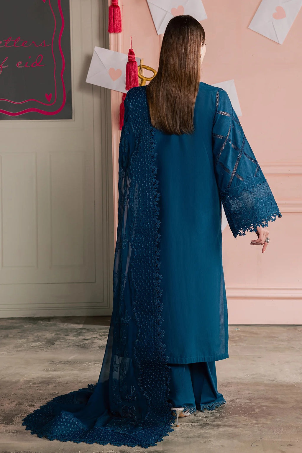 Woman wearing a blue lace dress standing in a room with pink walls and decorative elements.