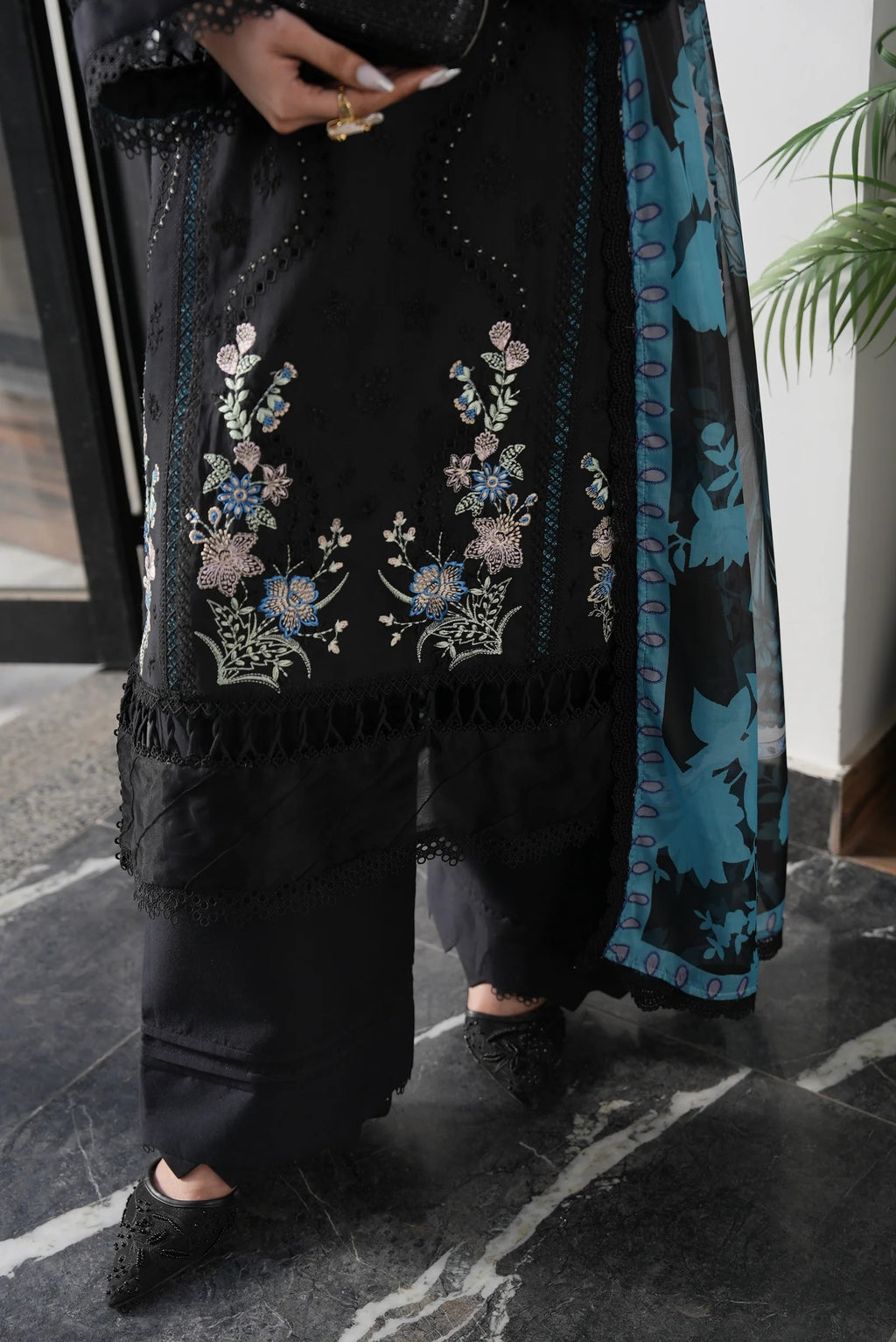 Person wearing a black embroidered outfit with floral patterns on a dark marble floor.