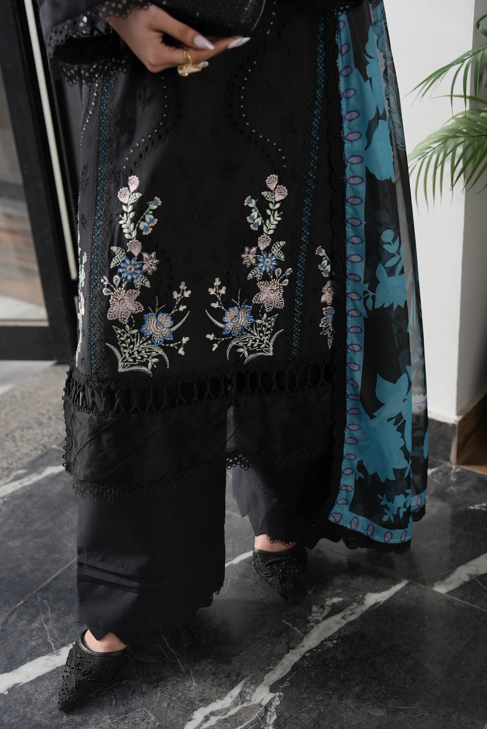 Person wearing a black embroidered outfit with floral patterns on a dark marble floor.