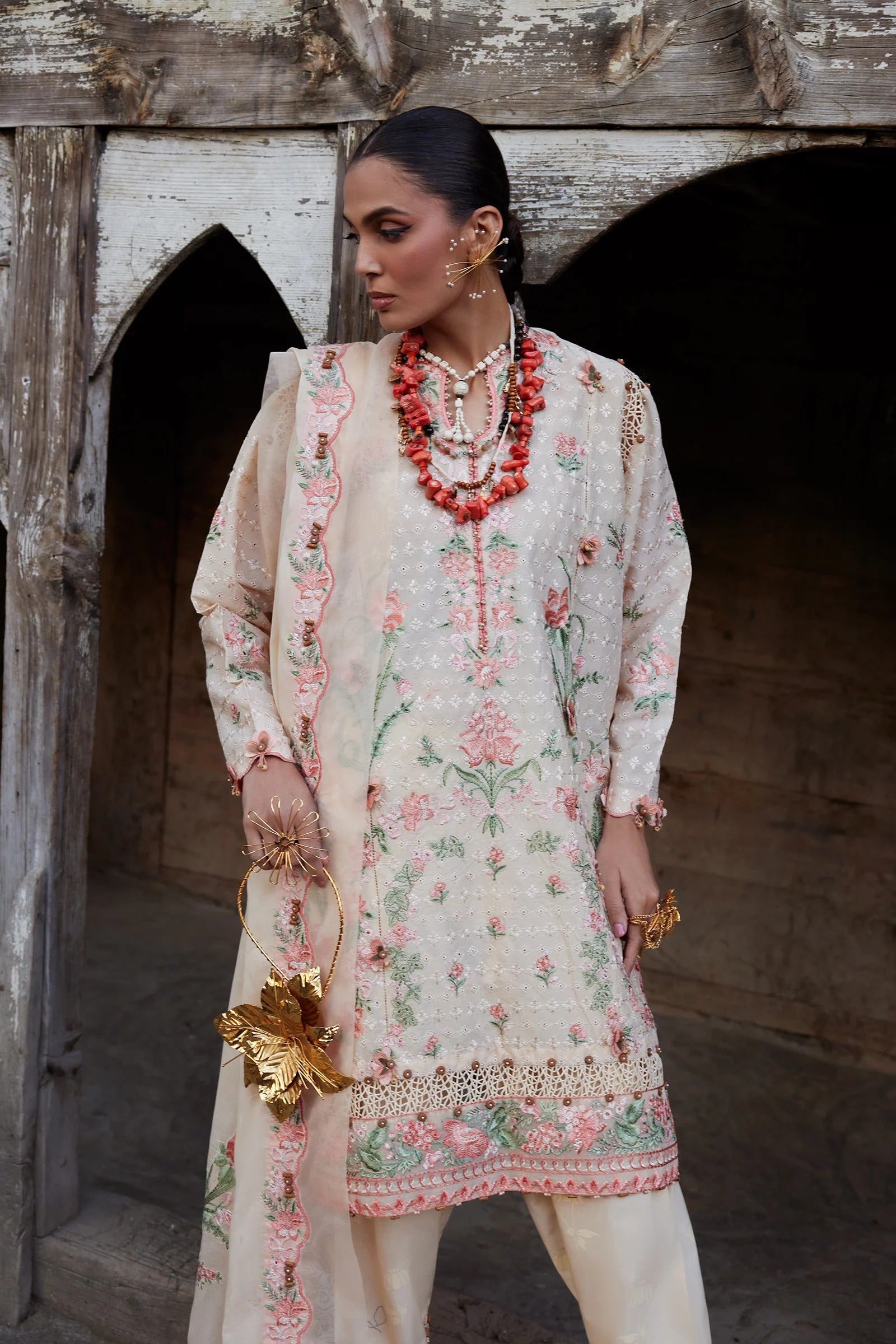Woman in traditional embroidered outfit with jewelry standing in a rustic setting