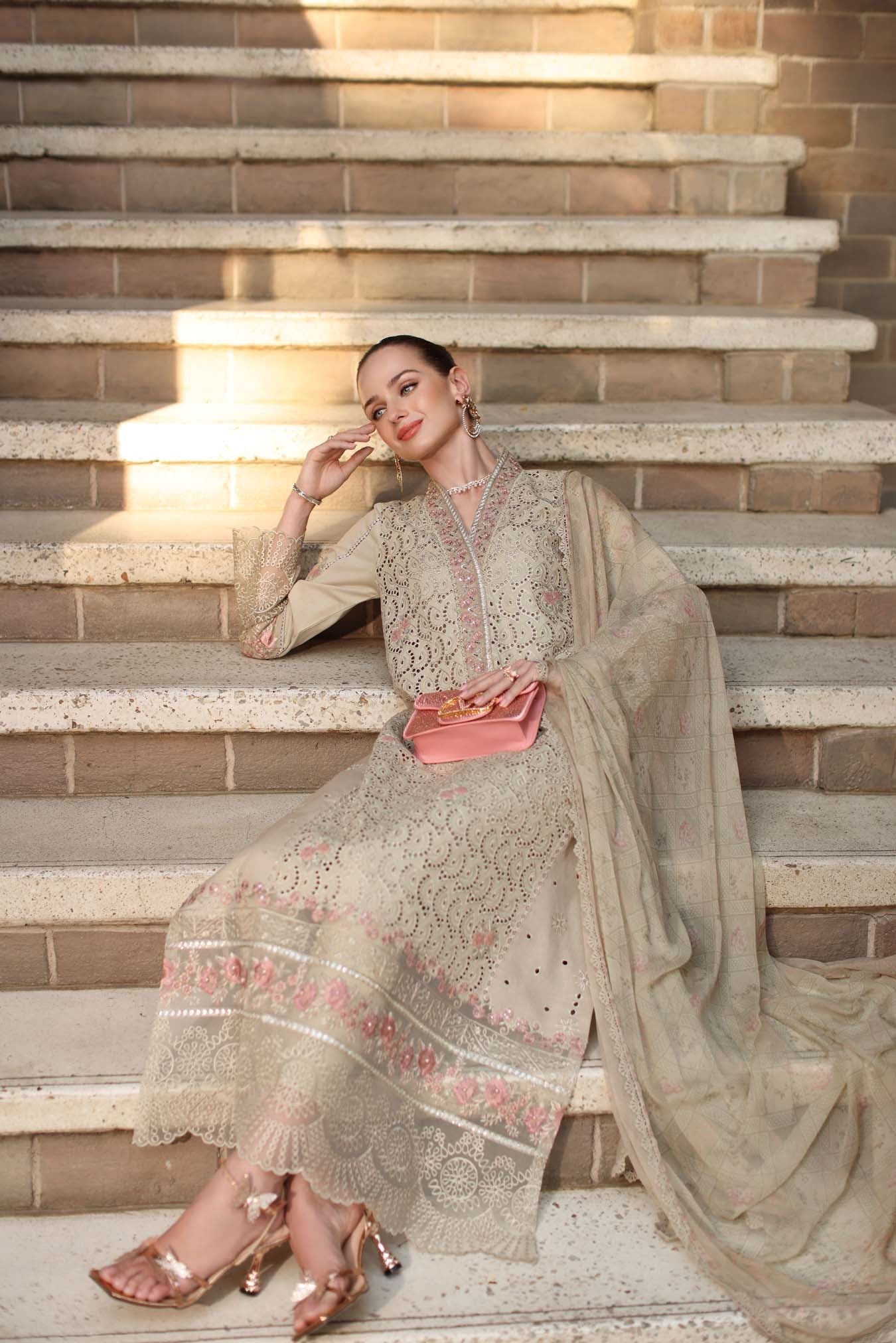 Woman in traditional outfit sitting on steps with a pink clutch