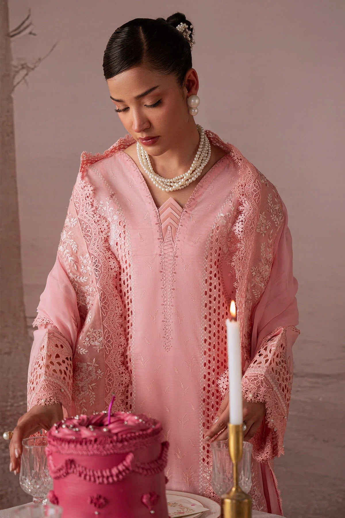 Woman in a pink traditional outfit with lace details, holding a lit candle and a pink container.