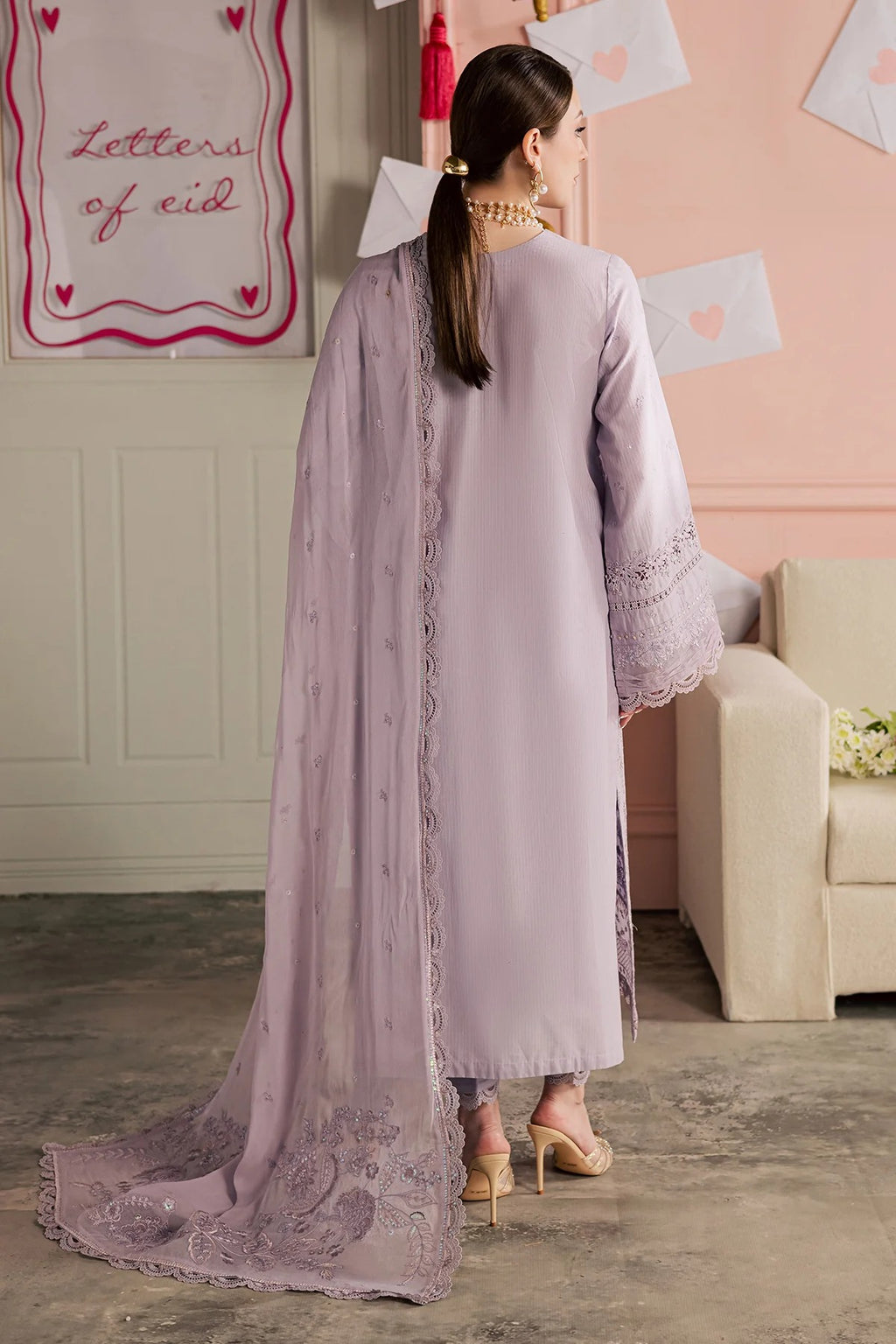 Woman in a light purple traditional outfit with a lace dupatta in a decorated room.