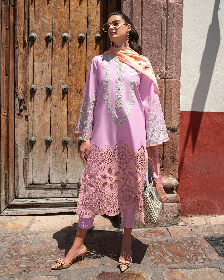 Woman in a pink dress with floral patterns standing in front of a wooden door.