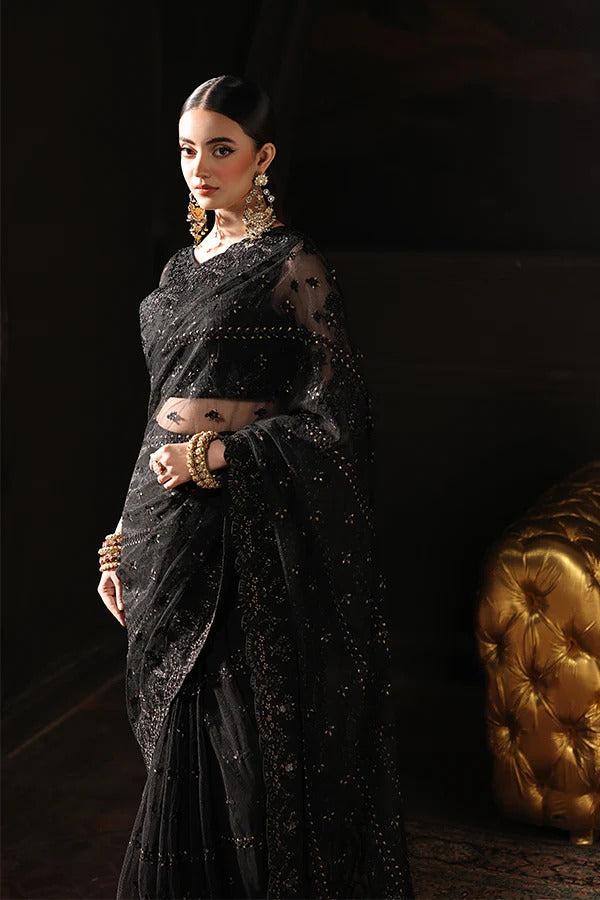 Woman in a black saree with gold jewelry against a dark background