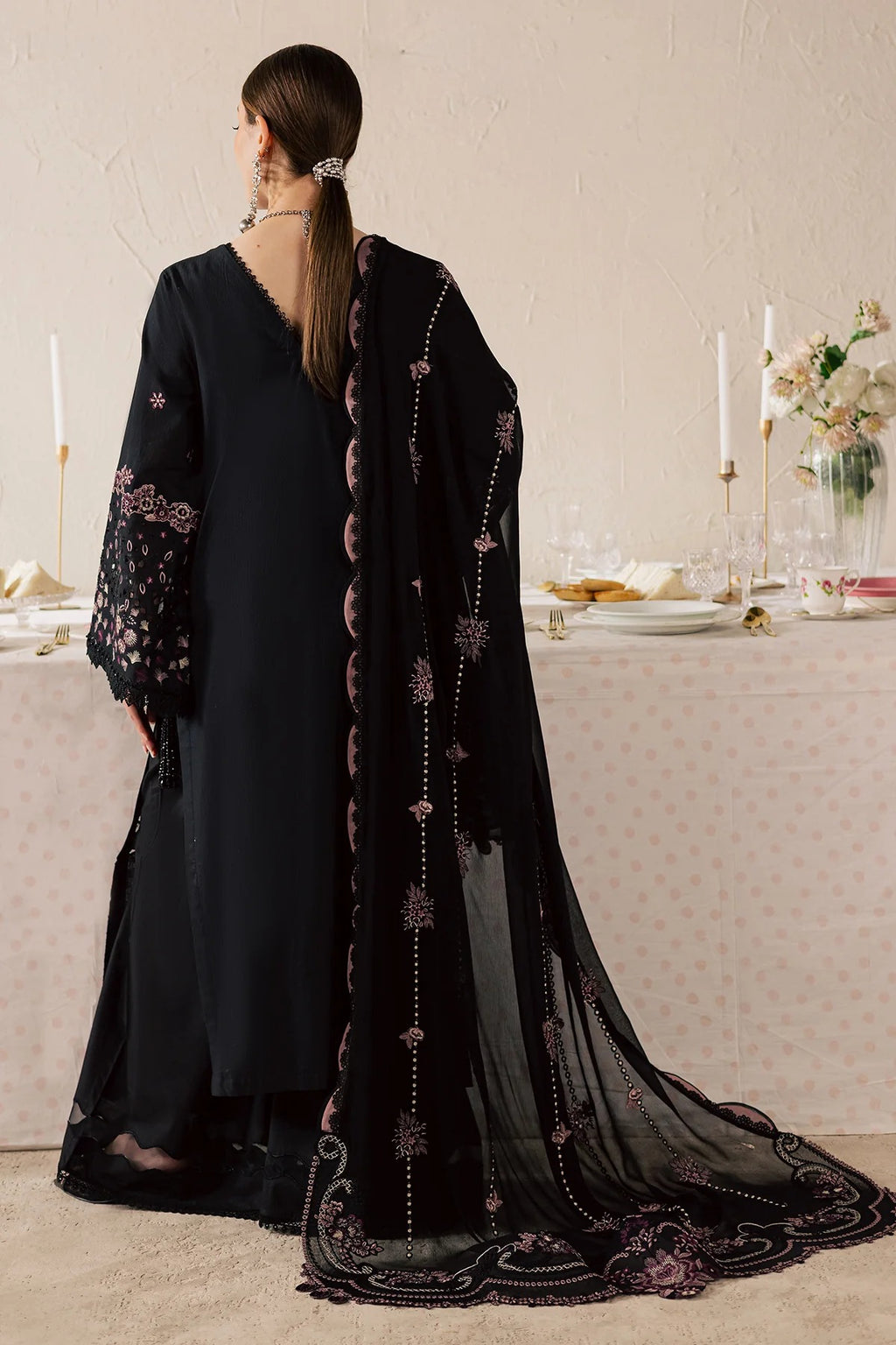 Woman wearing a black dress with floral embroidery in a formal setting.