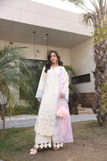 Woman in a white traditional outfit with a pink shawl standing outdoors.