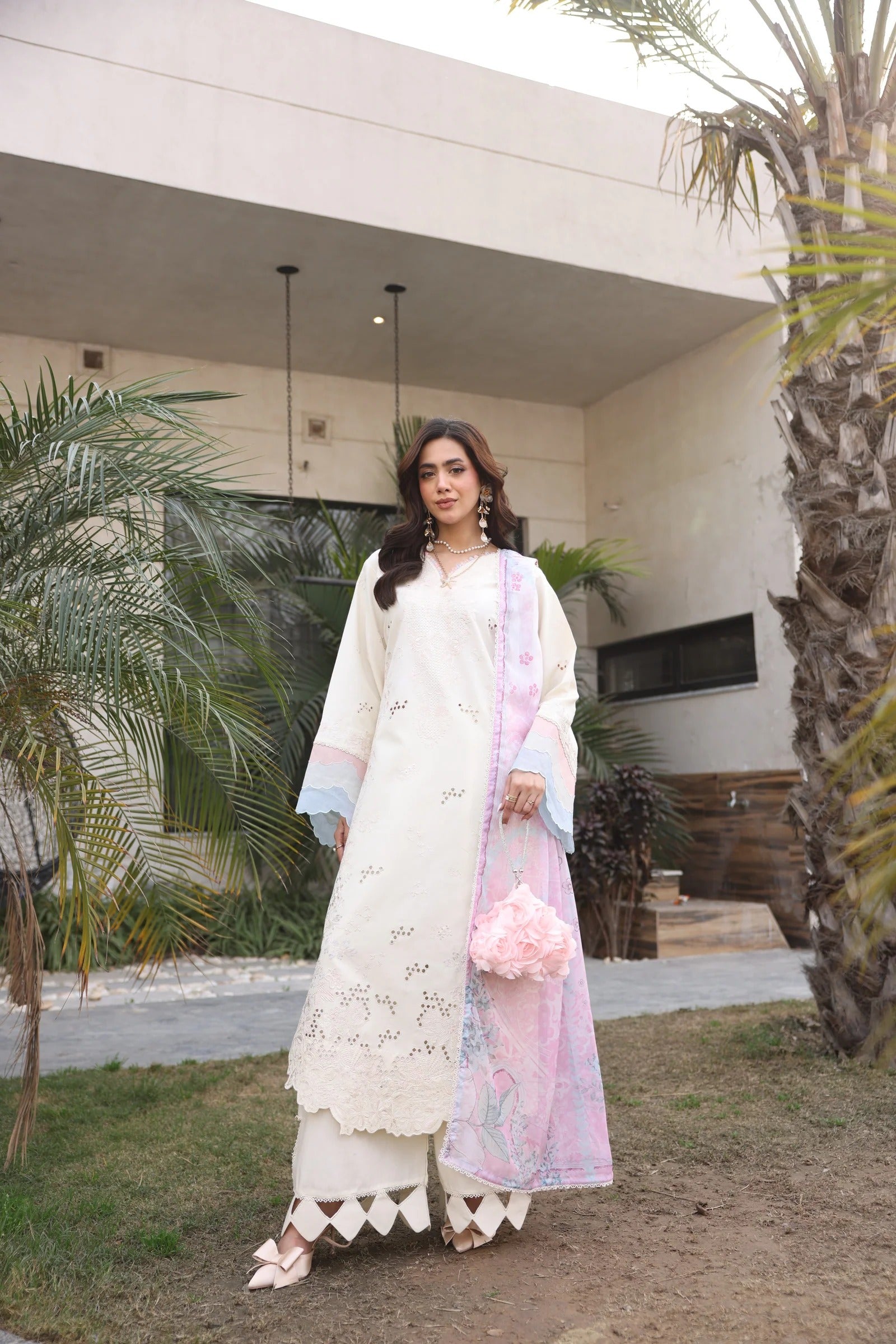 Woman in a white traditional outfit with a pink shawl standing outdoors.
