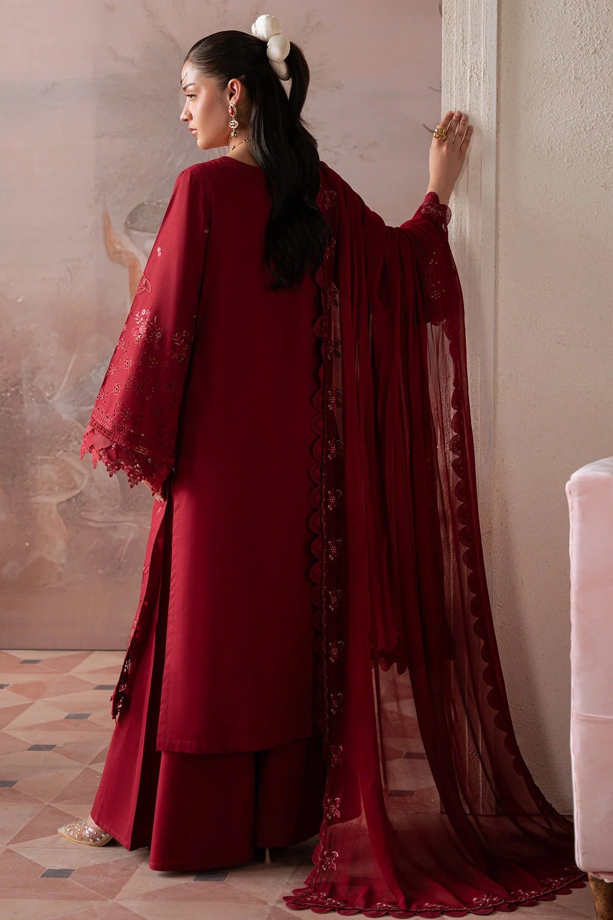 Woman in a red traditional outfit with a matching dupatta, standing against a neutral wall.