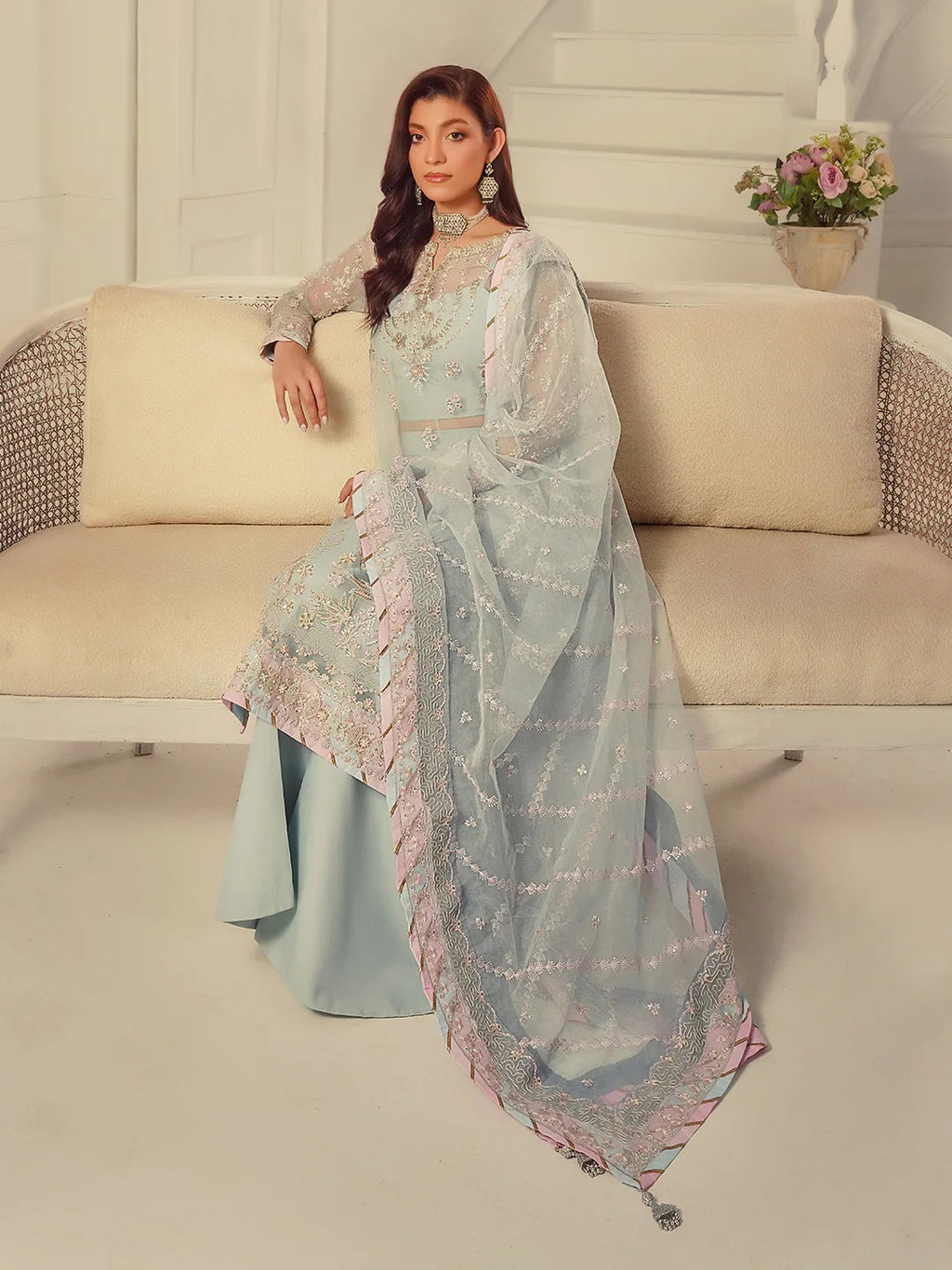 Woman in a light blue traditional outfit sitting on a beige sofa in a well-lit room.
