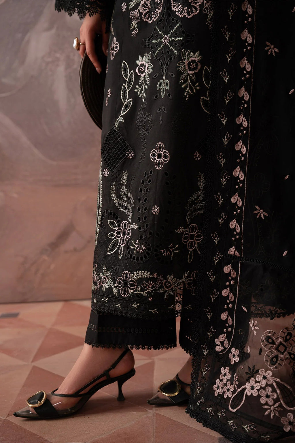 Black embroidered dress with floral patterns on a textured floor.