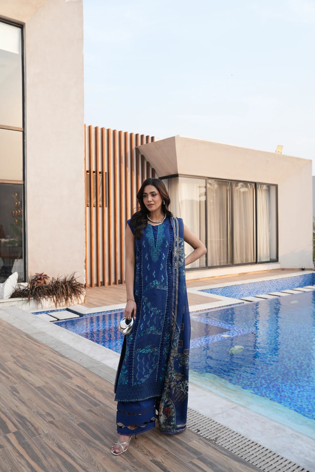 Woman in a blue dress standing by a pool with modern architecture in the background