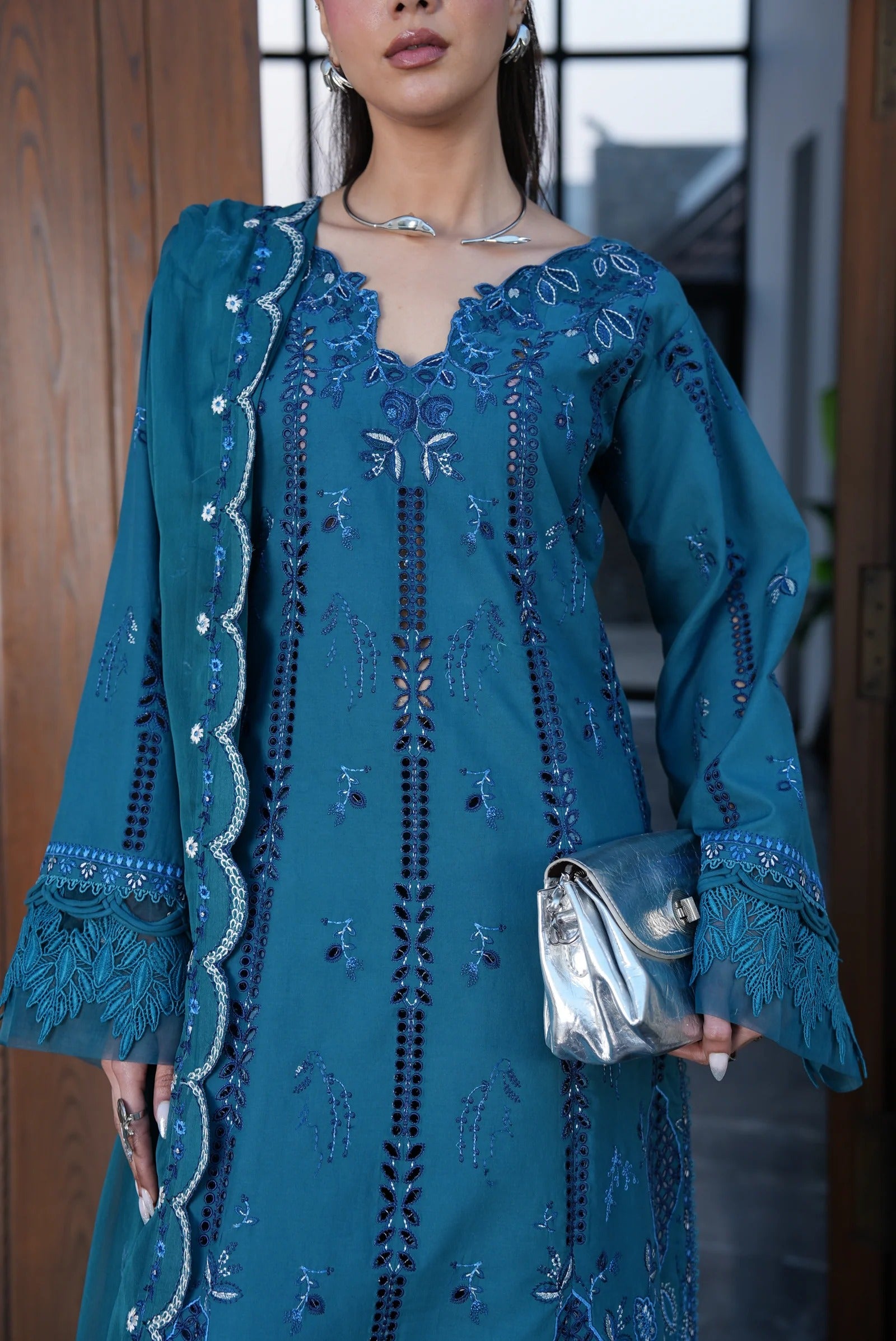 Woman wearing a blue embroidered dress holding a clutch.