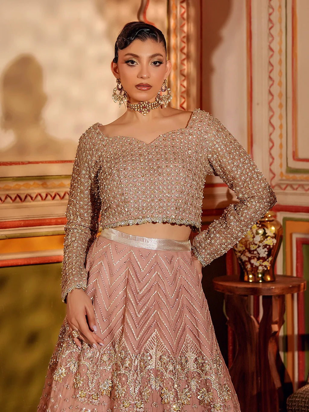 Woman wearing a traditional outfit with intricate designs in a decorated room.