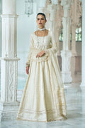 Woman in a traditional cream outfit standing in an elegant interior setting.
