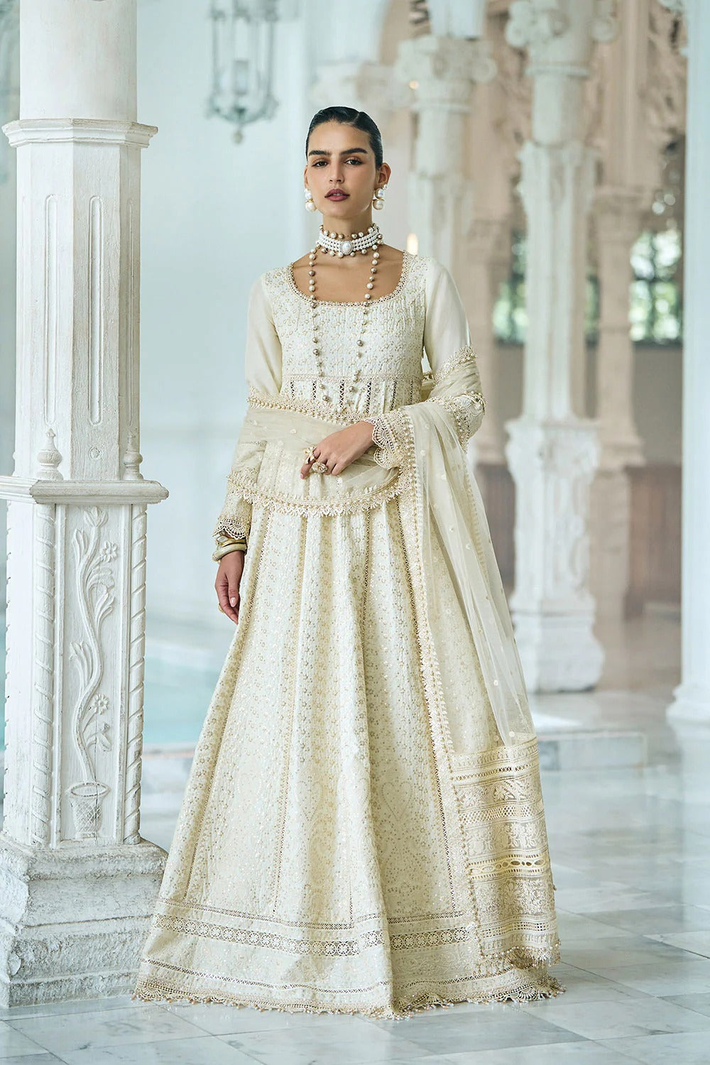 Woman in a traditional cream outfit standing in an elegant interior setting.